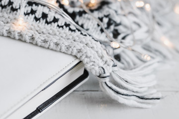 White book and knitted blanket with lights for home decoration on wooden table. Reading at home concept. Cosy atmosphere