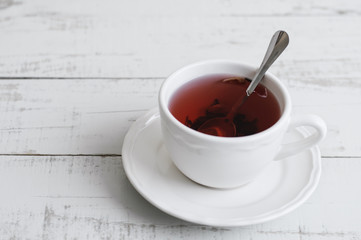 Red hibiscus tea in a small white cup with a metal spoon on wooden background. Tea break