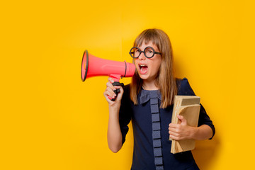 Portrait of a nerd girl in glasses with books and megaphone on yellow background