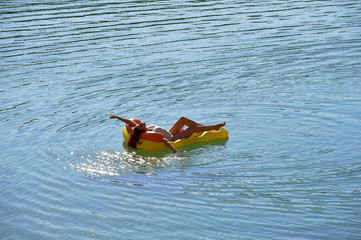 A beautiful young woman relaxes on an inflatable  sun bed in the middle of a lake. She wears a...