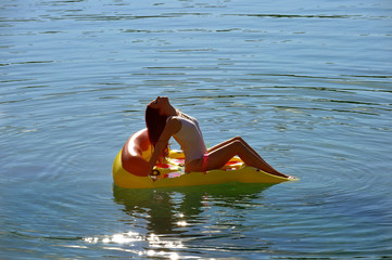 A beautiful young woman relaxes on an inflatable  sun bed in the middle of a lake. She wears a...