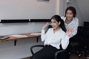 Two playful young Asian business women playing together with chair in office.