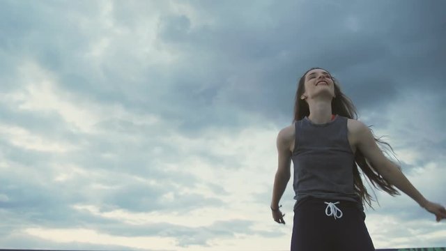 Young sexy hip hop girl dances in front of a sunset blue sky with clouds