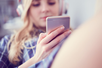 Beautiful Caucasian girl in headphones is listening to music, using a smart phone and smiling while lying on couch at home