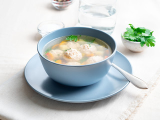 soup with meatballs in blue plate, white linen tablecloth and napkins, light background, side view