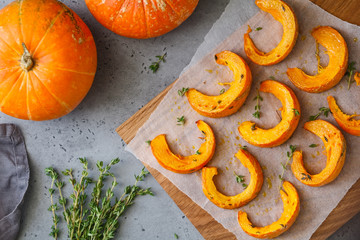 Baked pumpkin slices with thyme on a wooden board over grey table. Seasonal food vegetarian recipe....
