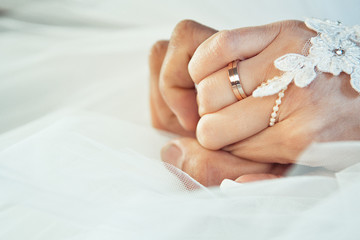 The bride and groom tenderly squeeze each other's palms. Wedding rings are visible