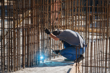 Welder works on welding of basement metall carcass