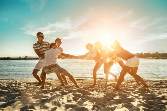 Friends funny tug of war on the beach under sunset sunlight 