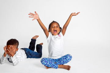 Young African American Sister and Brother the Girl is an Obvious Extrovert with Mouth Open and Hands in the Air The Boy is Hiding Behind His Hands Like an Introvert