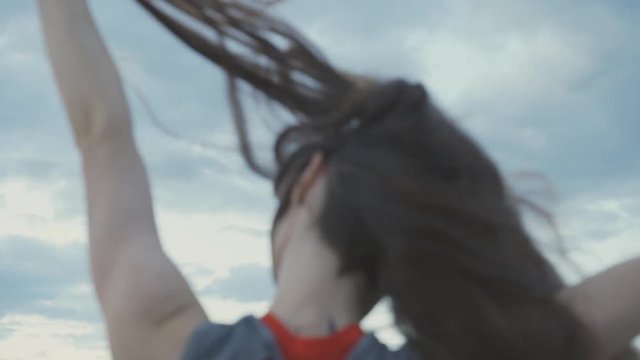 Teenager dances, filmed from behind, waving her hair into the sky  