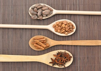 Concept with ingredients for chocolate, cocoa beans, cinnamon, anise, apricot beans on wooden spoons on brown background, top view