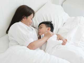 Beautiful asian mother watching her son sleeping in bed at home. Lovely mother putting son to the bed. Happy family concept.
