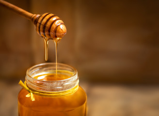 Honey in a glass jar with honey dipper on rustic wooden table background. Copy space.