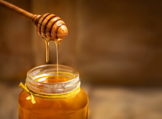 Fototapeta na wymiar Honey in a glass jar with honey dipper on rustic wooden table background. Copy space.