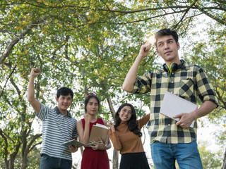 Handsome young asian college student holding notebook and illuminated light bulb while his friends standing on background. Idea,education, inspiration concept.