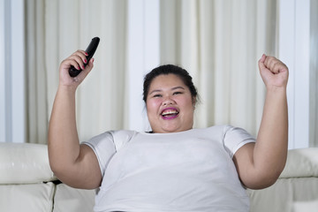 Happy overweight Asian woman clenched her fists while holding a remote control