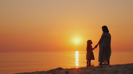 A pregnant woman with a daughter is standing on the beach at sunset. Waiting for the second child