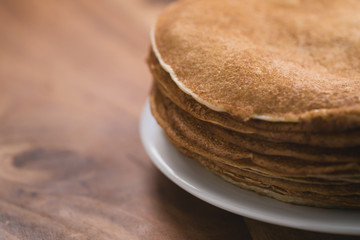 Stack of fresh hot crepes or blinis on wood table with copy space