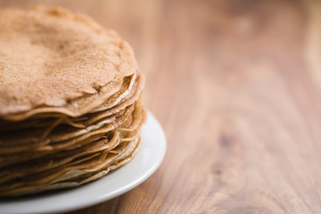 Stack of fresh hot crepes or blinis on wood table with copy space