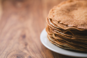 Stack of fresh hot crepes or blinis on wood table with copy space