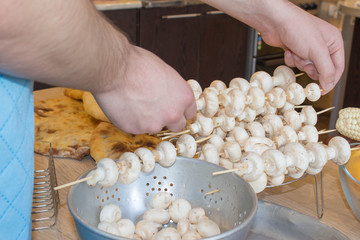 A man hand puts pieces of mushrooms on skewer. mushrooms on skewers