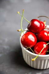Fresh ripe cherries in small white ceramic bowl on the rustic background. Selective focus. 