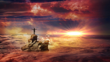 A man with spread arms standing on a rock protruding above the clouds and looking at a flare on the horizon.