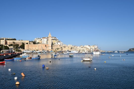 Marsaskala harbour with boats and dishing vessels and church in the distance
