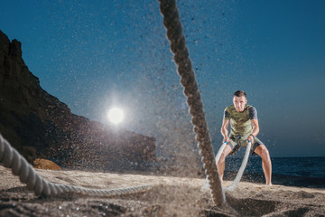 Man training with battle rope on the beach. Athlete doing cross fitness workout outdoor. Sport fit...