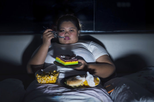 Overweight woman eating junk food in bed before sleeping