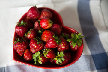 Strawberries in a red heart shaped bowl.
