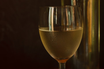 Glass of white wine, bottle of white wine on vintage wooden background. Close-up, selective focus.