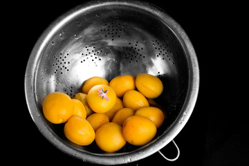 Washed apricots in a colander, on a black background.