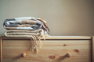stack of beige checkered wool blankets on a wooden chest. autumn - winter concept of home warmth...