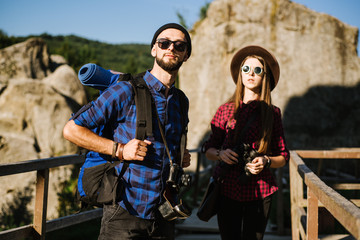 Fototapeta na wymiar A couple traveling by the mountains wearing hipster clothes with backpack, vintage camera and binoculars