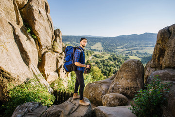 A traveler man with big backpack standing on the rocks and looking forward