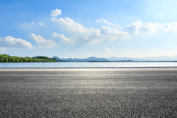 Empty asphalt road and lake with mountains on a sunny day