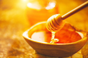 Honey dripping from honey dipper in wooden bowl. Healthy organic thick honey pouring from the wooden honey spoon closeup