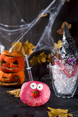 Dishes with glazed donuts, with a red cocktail in a glass tube in a bucket of ice, in the background of a spider, a pumpkin face and a spider's web for a Halloween party