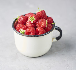 Fresh and ripe raspberry in mug, green leaves