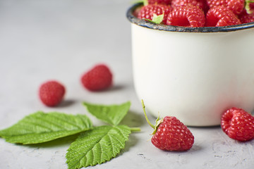 Fresh and ripe raspberry in mug, green leaves