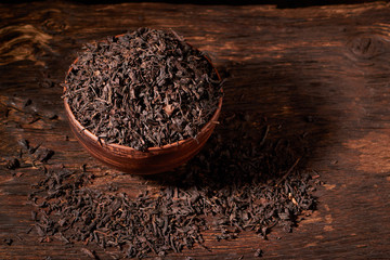 Dried black tea in clay bowl with sticks of cinnamon and a tea strainer isolated on black background