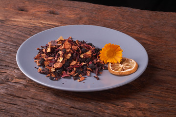 Black dry fruit tea leaves in blue plate on wooden table. Selective focus