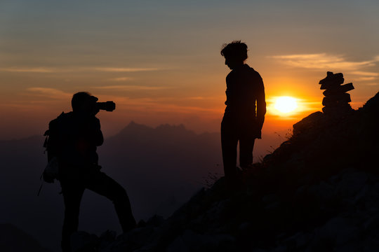 Photographer performs photography to a girl at sunset in high mountains in silhouettes