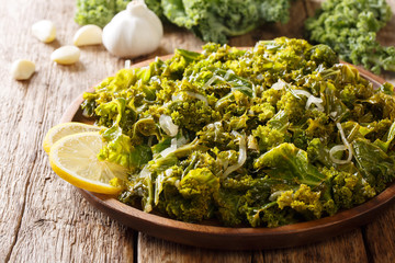 Kale leaf stew with onions, garlic, olive oil and lemon close-up on a plate and ingredients. horizontal