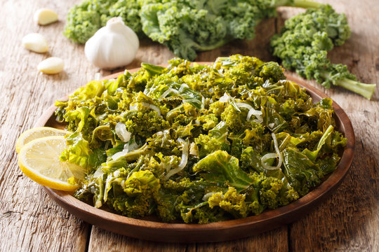Portion kale of leaf cabbage cooked with onions, garlic, oil and lemon close-up on a wooden background. horizontal