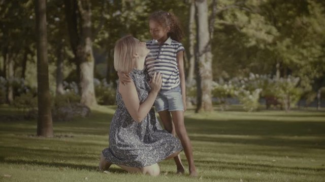 Affectionate beautiful caucasian mother bonding with her cute litte mixed race daughter in summer park. Happy family embracing, kissing while spending great time together on summer holidays outdoors.