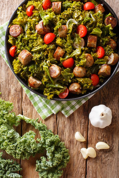 Fried kale cabbage with sausage, tomatoes and parmesan cheese on a plate close-up. Vertical top view