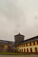 A rainy view of a castle watch tower with clouds and yellow buildings
